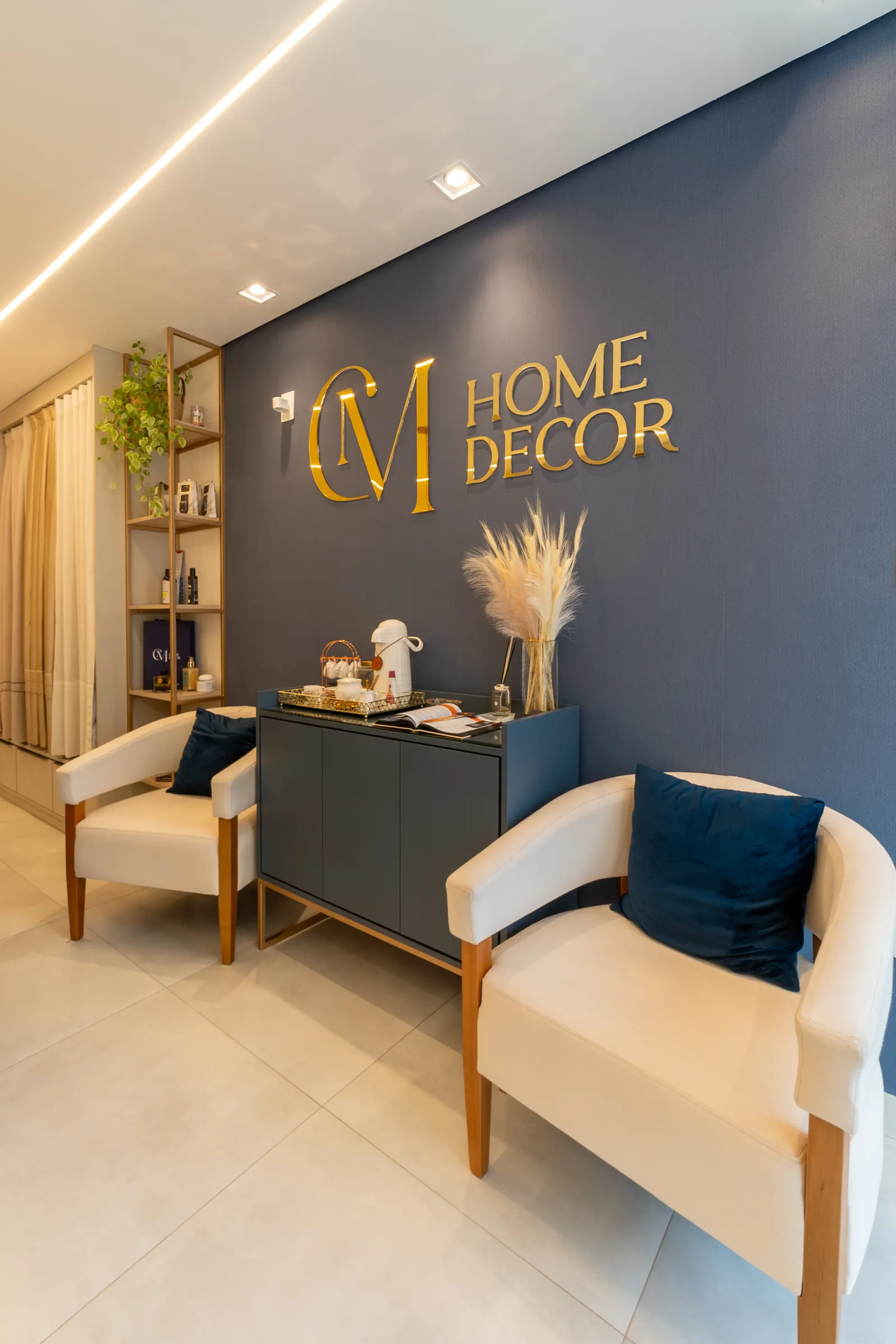 Parede azul com o logo dourado da CM Home Decor e poltronas